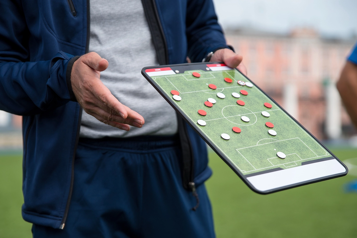 Person zeigt Fußball-Taktik auf einem Taktiktafel mit Spielfiguren.